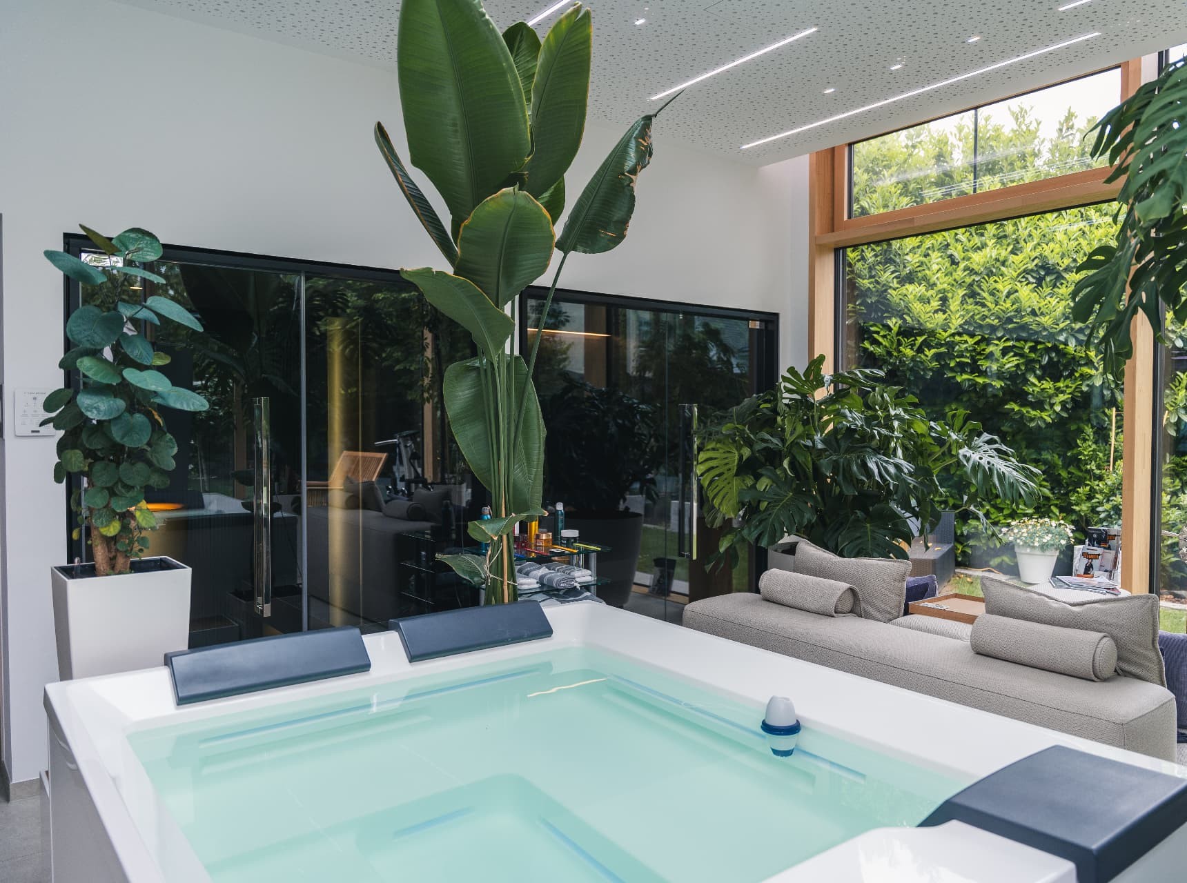 Lichtdurchfluteter Innenraum der Academy mit Whirlpool, Pflanzen und Blick in den Garten