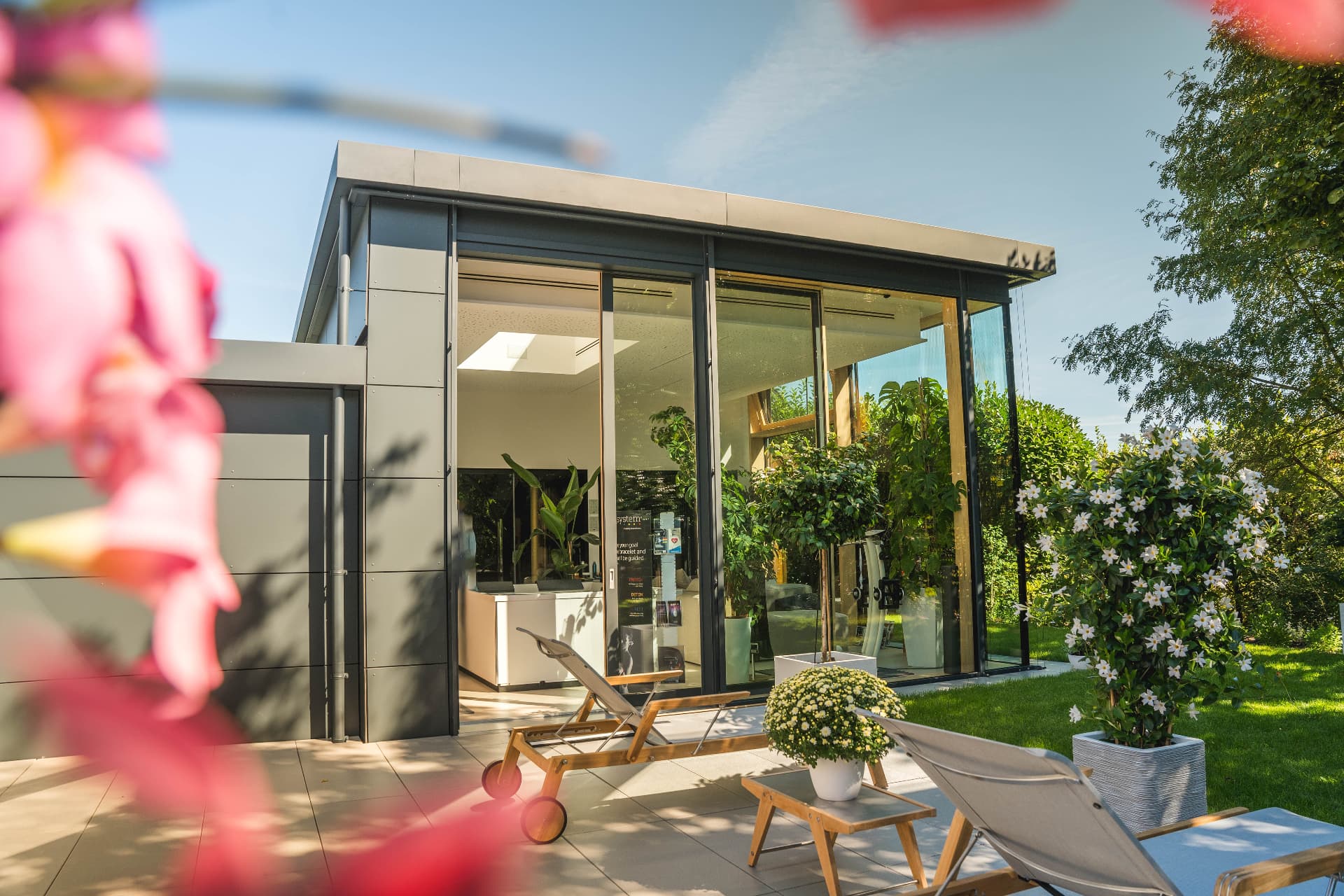 Die gläserne Vitalität Academy mit Terrasse und Garten bei Sonnenschein